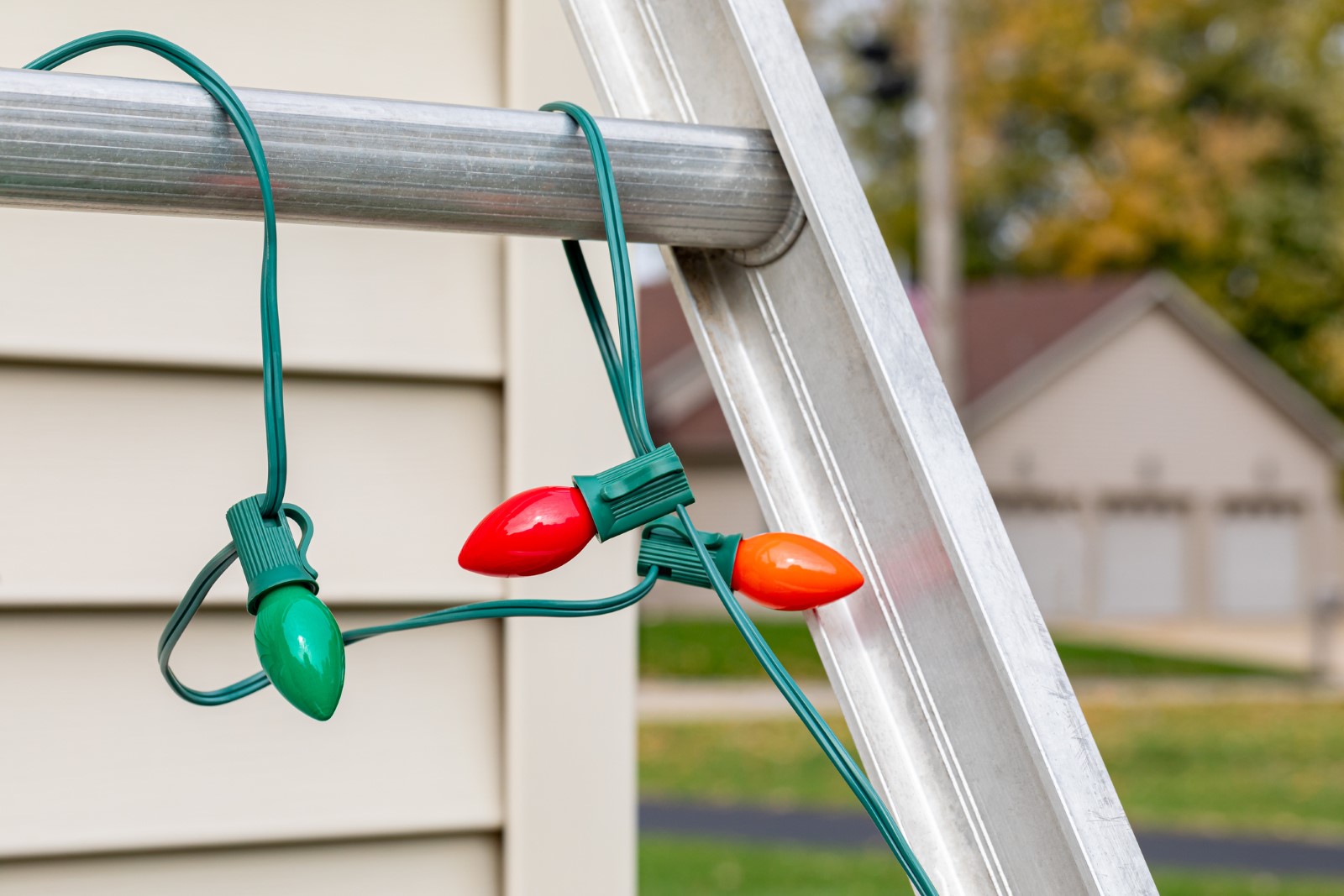 Christmas string lights hanging on ladder rung outside of house. Holiday lighting decorating, ladder safety and accident prevention concept.